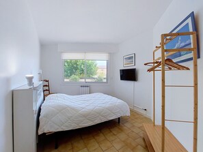 Un dormitorio pequeño y bien iluminado con cama, ventana, televisor y armario de madera.