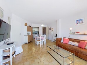 Una sala de estar moderna con una televisión, una mesa de centro de vidrio, un sofá de cuero marrón y un comedor con una mesa y sillas.