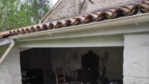 Een terras buiten, met een stenen muur, een tegeldak en een eettafel met stoelen.