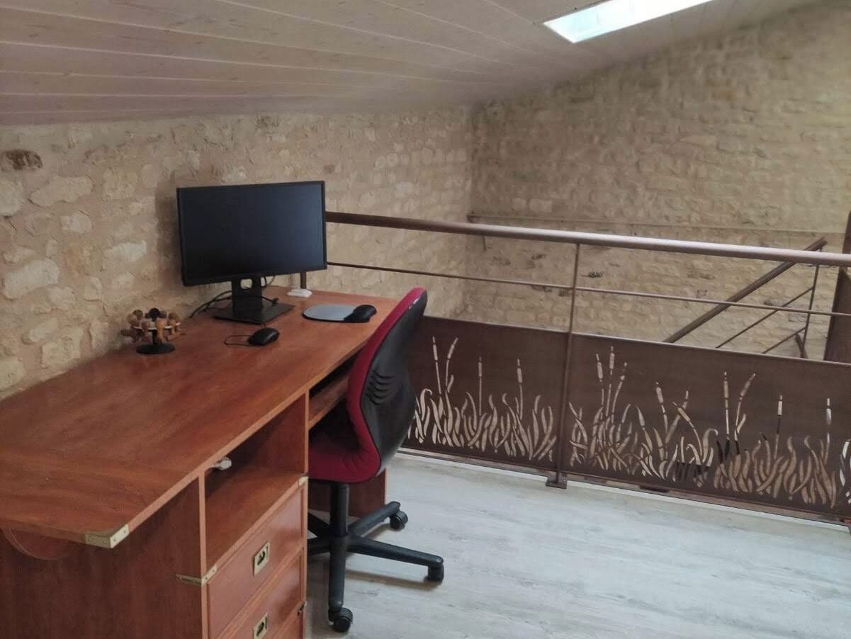 A room with a wooden desk, a computer monitor, and a red office chair.