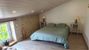 Een slaapkamer met een stenen muur, een bed met groen beddengoed, twee nachtlampjes, een raam met uitzicht en een houten vloer.