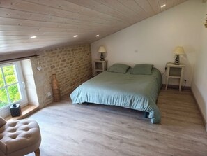 Ein Schlafzimmer mit Steinwand, einem Bett mit grüner Bettwäsche, zwei Nachttischlampen, einem Fenster mit Aussicht und einem Holzboden.