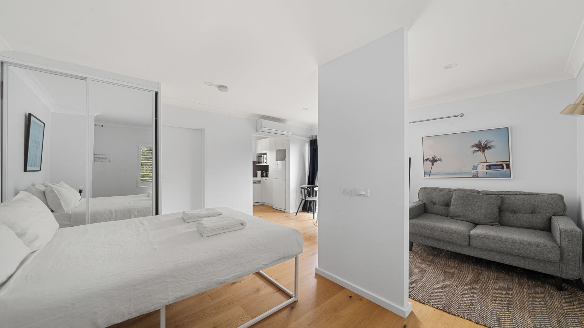 Ein modernes Schlafzimmer mit Bett, begehbarem Kleiderschrank und Blick in einen Küchenbereich.