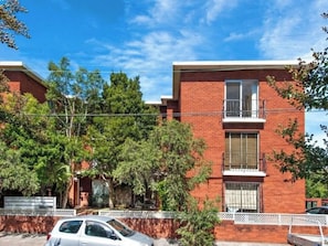 A two-story brick building with a balcony on the second floor, surrounded by trees and a white fence. - Sun Drenched 1 BDR Studio Apt in Newtown (Newtown)