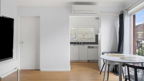 Una cocina moderna con lavavajillas incorporado, un comedor con mesa y sillas redondas, y un ventanal con persianas.