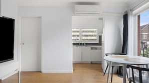 Eine moderne Küche mit eingebautem Geschirrspüler, ein Essbereich mit rundem Tisch und Stühlen sowie ein großes Fenster mit Jalousien.