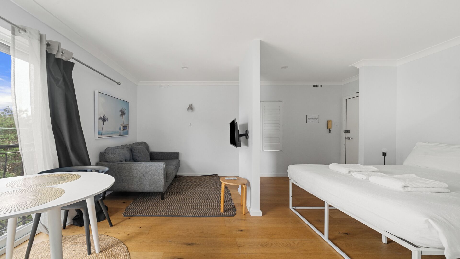 Ein modernes, helles Zimmer mit einem weißen Bett, einem grauen Sofa und einem kleinen Tisch.