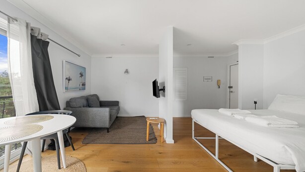 Una habitación moderna y luminosa con una cama blanca, un sofá gris y una mesita.