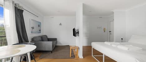 A modern, well-lit room with a white bed, grey sofa, and a small table.