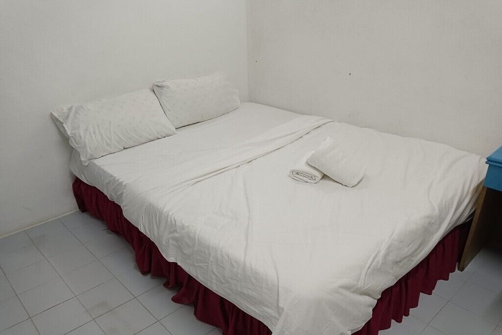 A single bed with a white mattress and red skirted base, a white pillow, and a folded white towel.