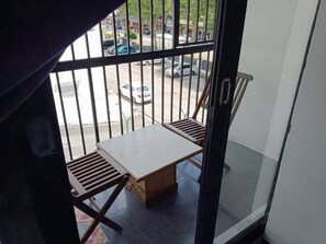 Un balcón con una mesa y dos sillas, vista a la calle, y una barandilla de metal.