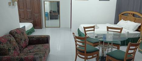 A room with a bed, a sofa, a dining table with chairs, a wardrobe, and two paintings on the wall.