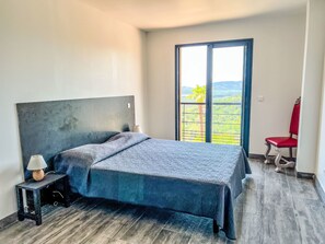 Ein Schlafzimmer mit einem Bett, einem Nachttisch, einem Sessel und einem großen Fenster mit Blick.