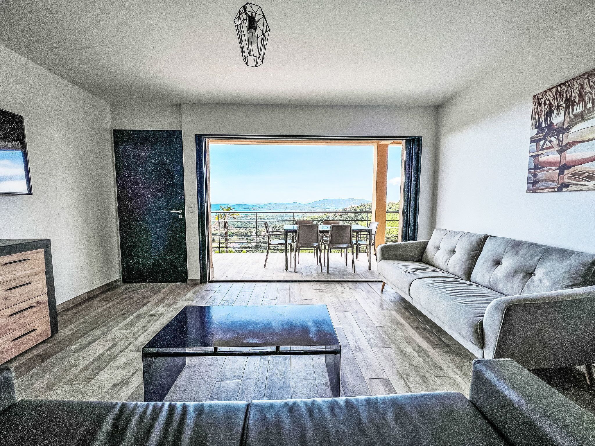Un salon moderne comprenant un canapé, une table basse et un coin repas avec des chaises. Une grande fenêtre offre une vue sur l’extérieur.