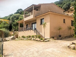 Ein zweistöckiges Haus mit Balkon und Treppe, eingebettet in eine umliegende Landschaft.