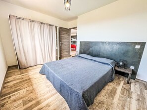 Une chambre à coucher comprenant un lit, une table de chevet, une chaise, une armoire et une salle de bain visible à travers une porte ouverte.