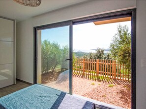 A bedroom with a large sliding glass door leading to a patio with a wooden fence and trees. - Dea Sole by Interhome (Sainte Lucie Porto Vecchio)