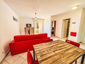 A living room with a red sofa, a wooden dining table, and a television on a cabinet. - Dea Alba by Interhome (Sainte Lucie Porto Vecchio)