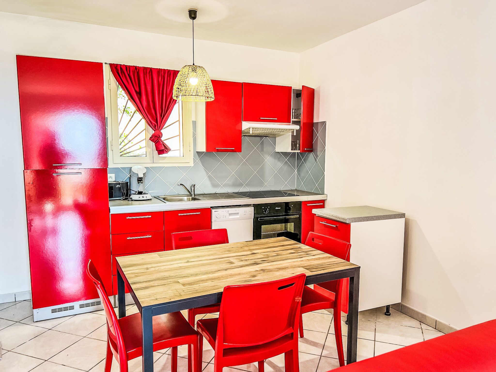 Uma cozinha compacta com armários vermelhos, uma mesa de jantar de madeira e um lustre.