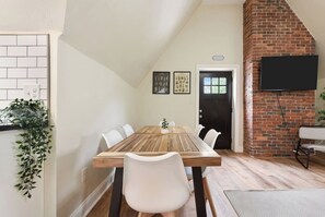Een eetgedeelte met een houten tafel en witte stoelen, een bakstenen muur en een zwarte deur.