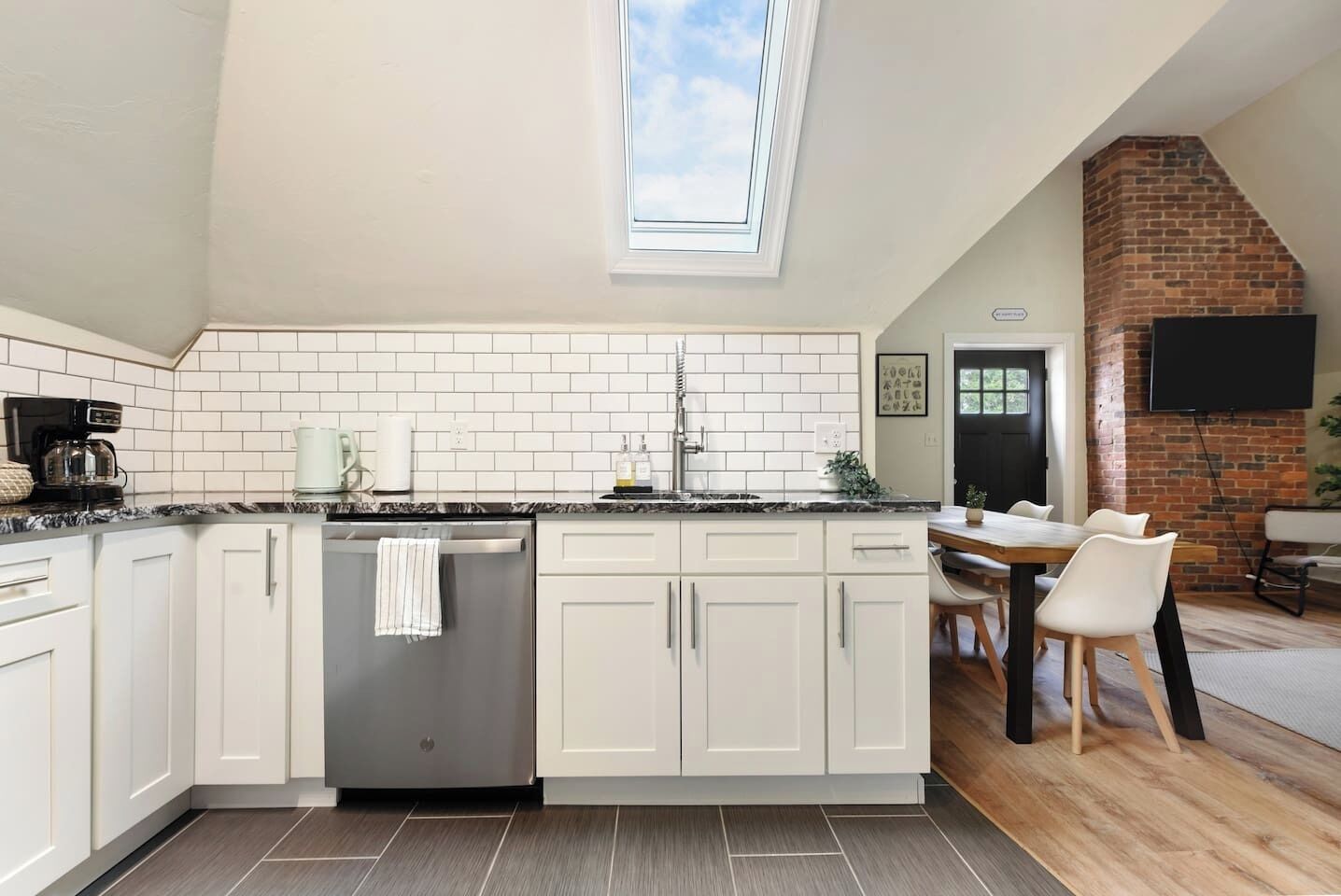 A modern kitchen with white cabinetry, a stainless steel dishwasher, and a skylight.