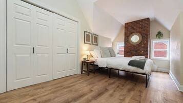 A bedroom with a bed, a nightstand, a lamp, a brick accent wall, and a large closet.