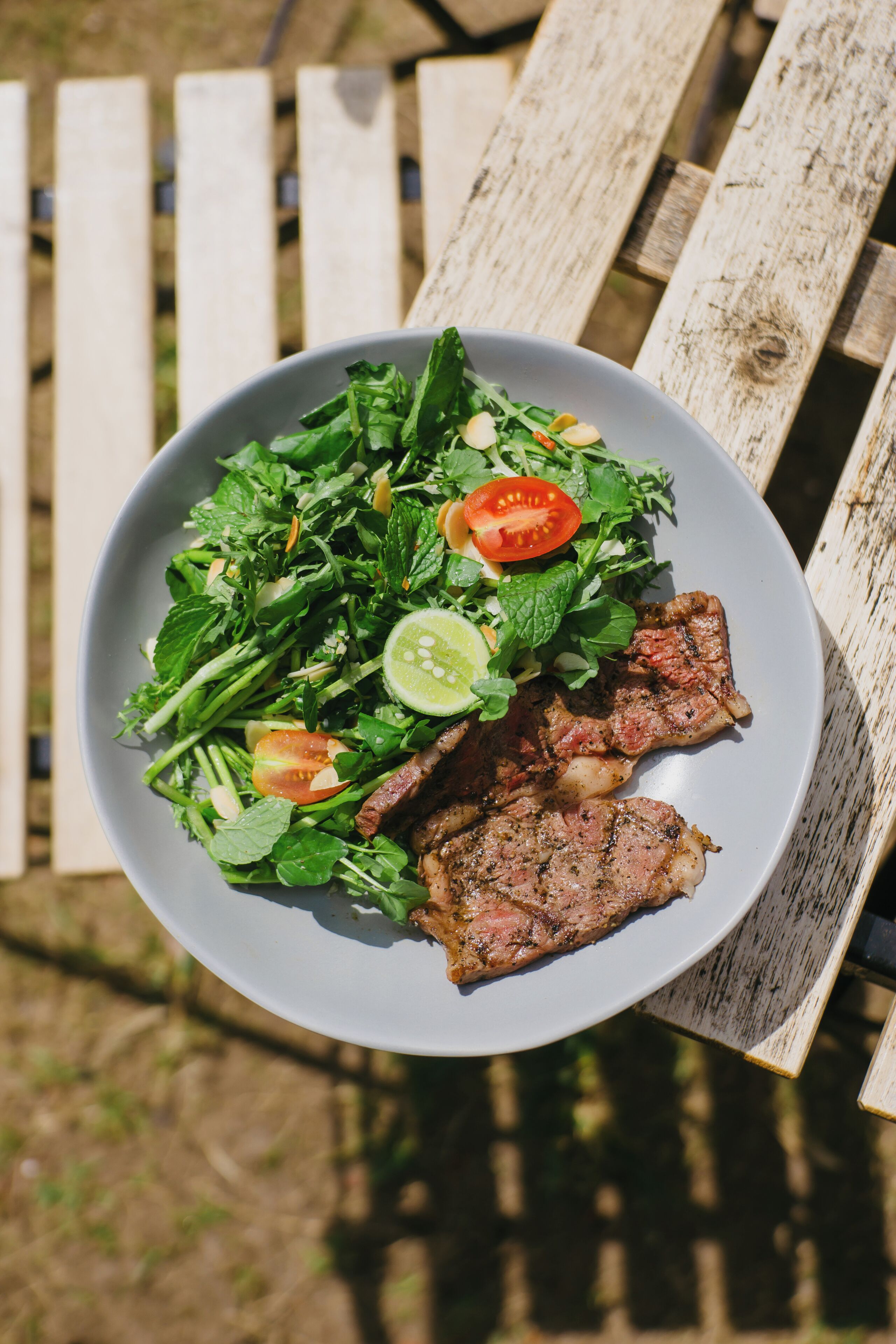 A plate of food with greens, tomatoes, and meat, placed on a wooden table.