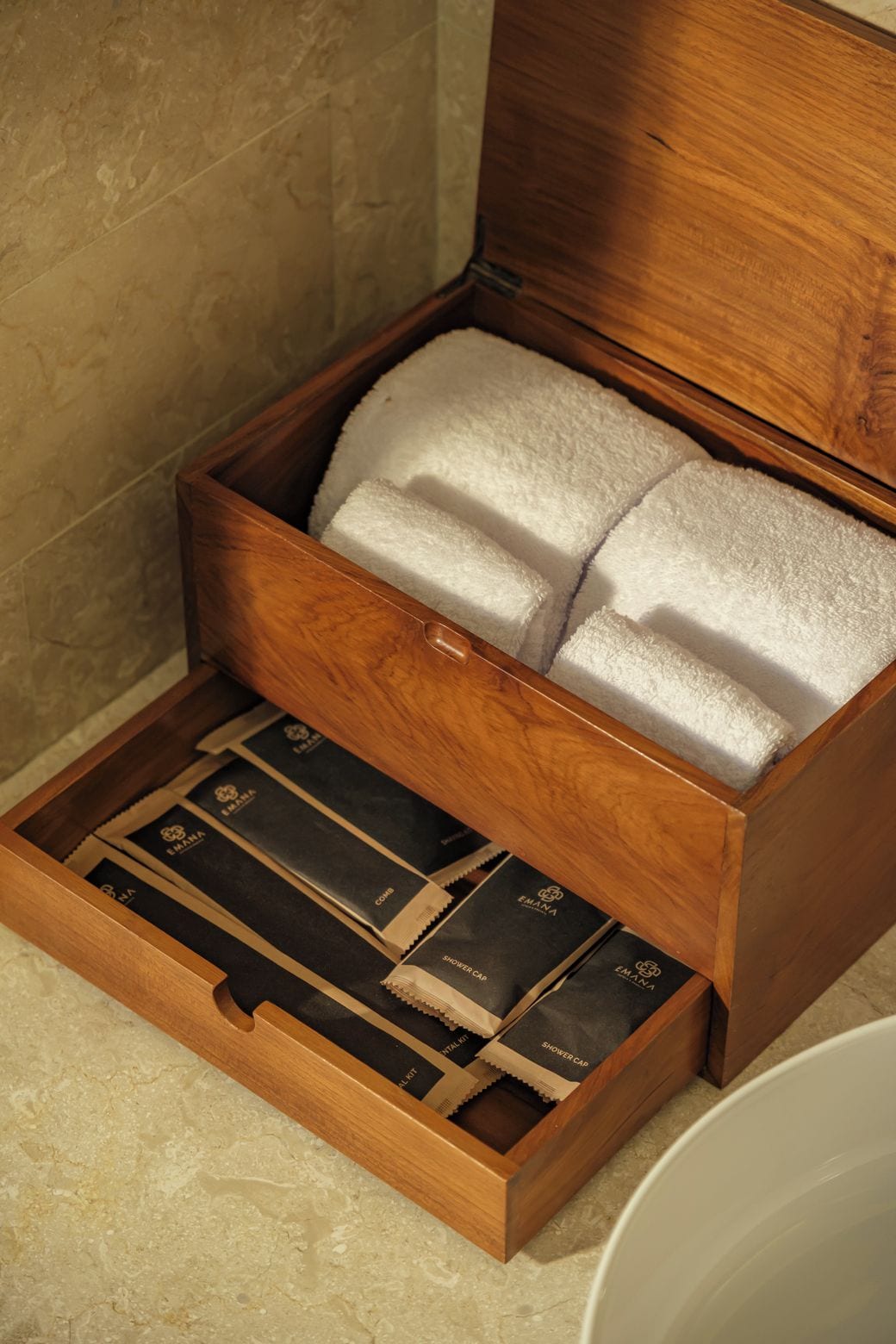 A wooden storage box with compartments containing white foam and black boxes labeled 'EMANA SHOWER CAPS.'