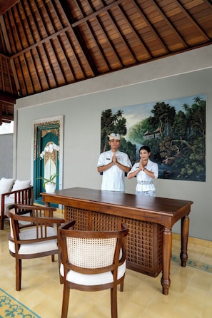 Una habitación con techo de madera, un cuadro de un paisaje tropical, una puerta tradicional y una mesa de comedor con sillas.