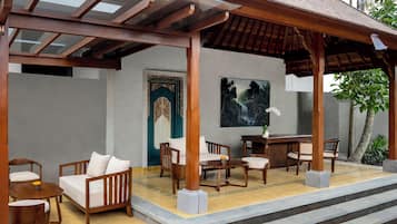 A covered outdoor seating area with wooden furniture, a door with intricate design, and a painting of a waterfall.