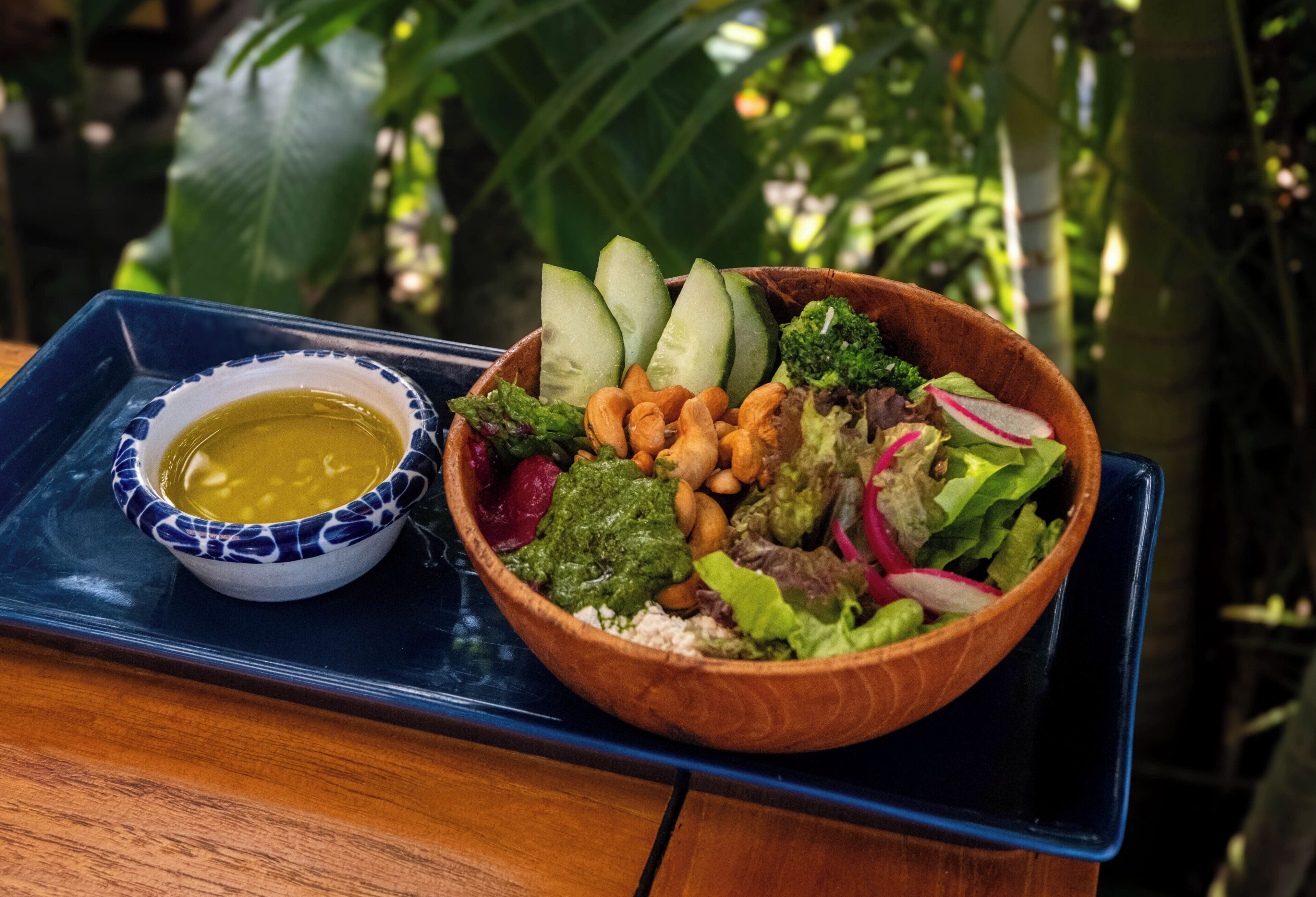 En træskål fyldt med salat og en lille skål med dressing på en blå bakke.