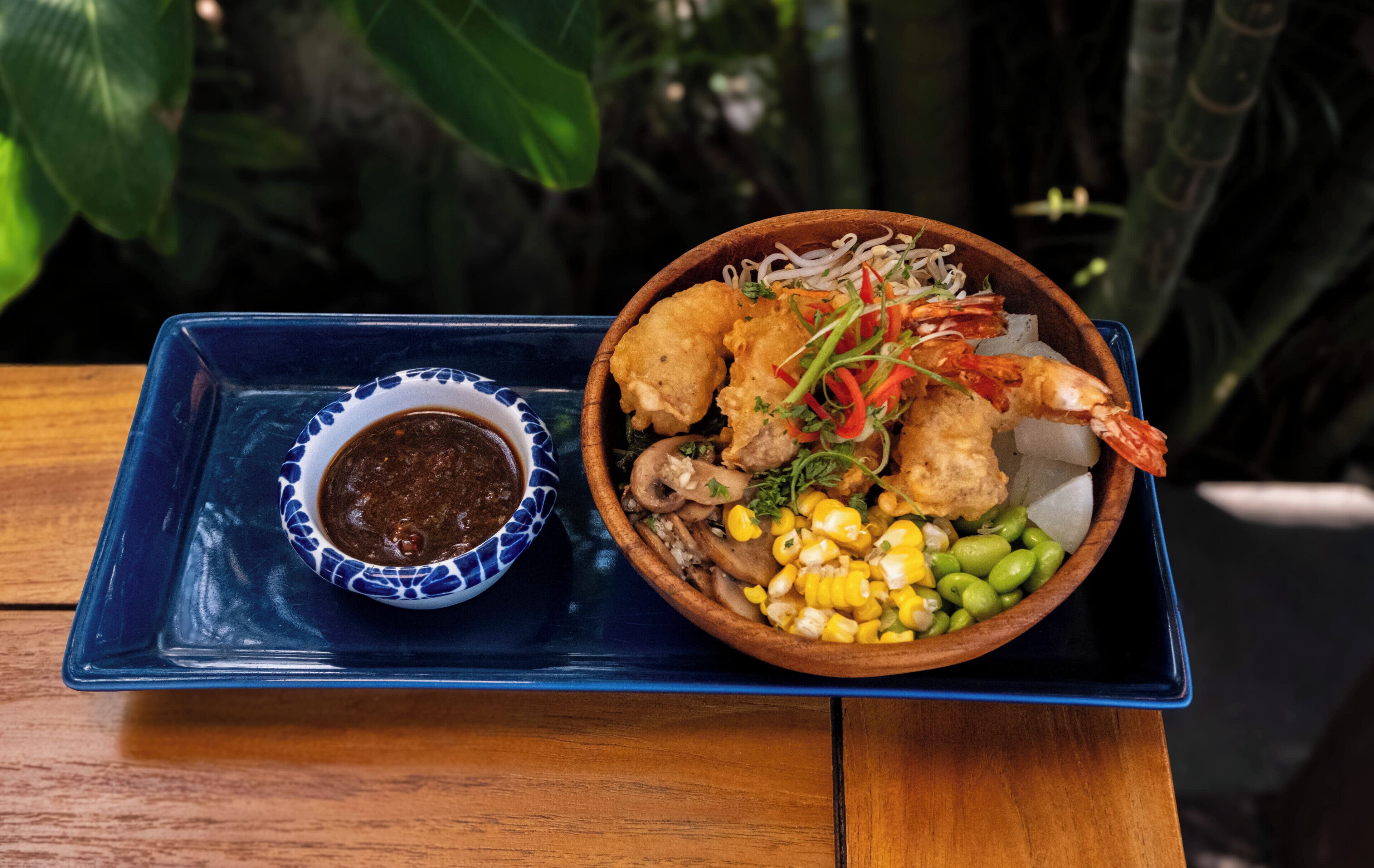 A meal consisting of fried shrimp, vegetables, and a side of sauce on a blue tray.