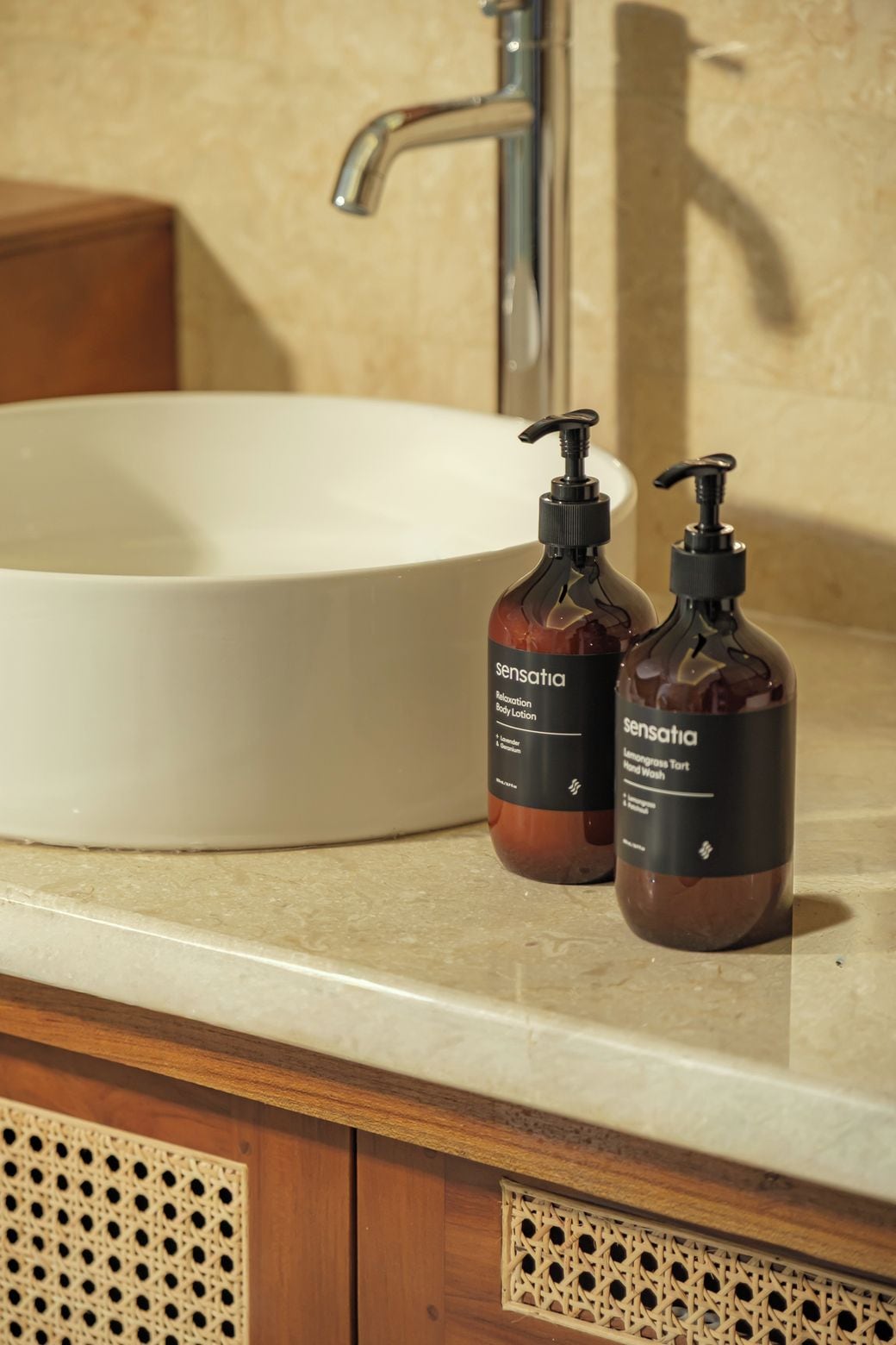 A bathroom sink with two bottles of Sensatia body lotion and hand wash on the countertop.