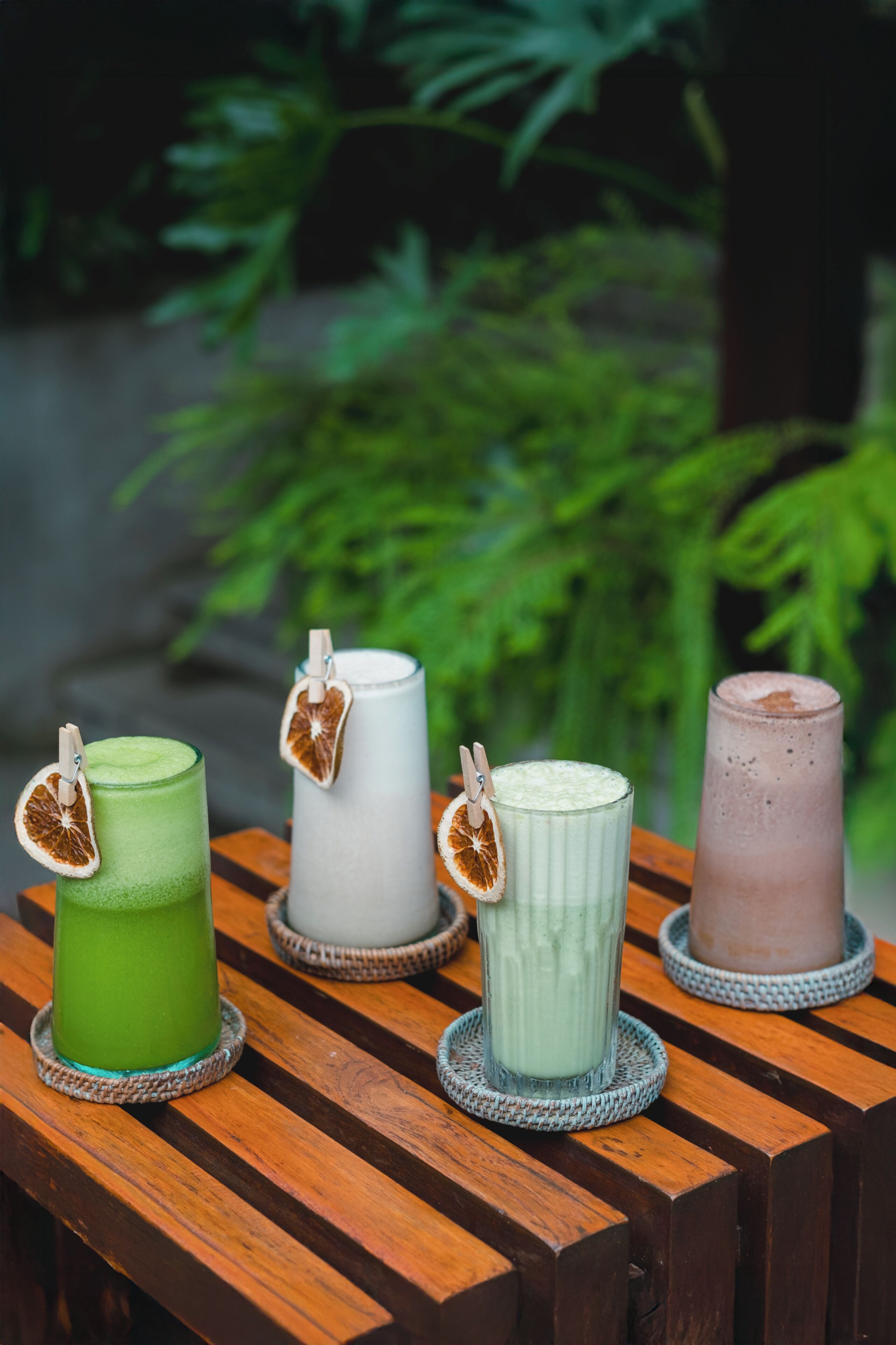 Four glass containers with clothespins holding dried orange slices, placed on a wooden surface with a blurred green background.