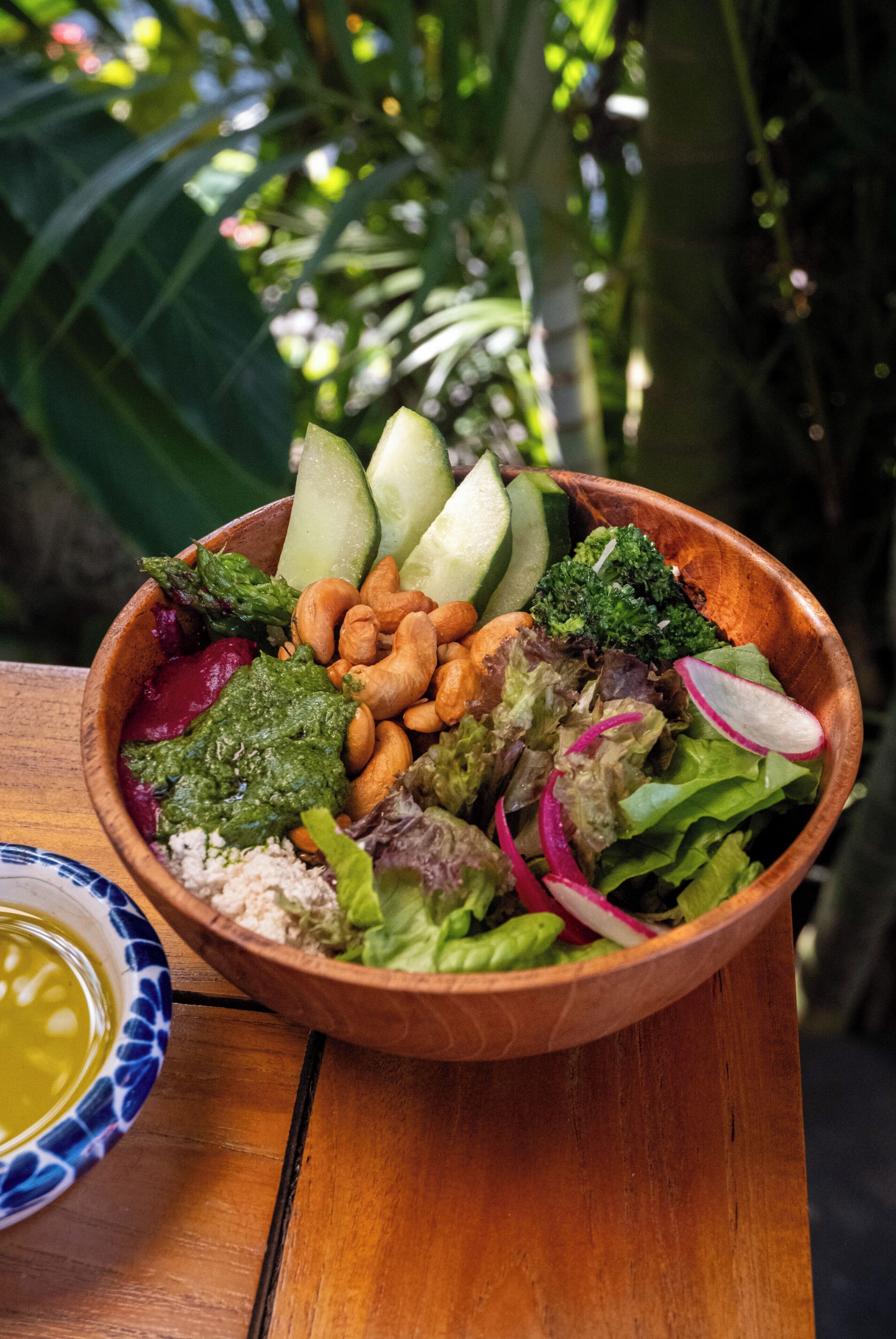 A wooden bowl filled with various salad ingredients on a wooden table.