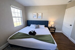 A bedroom with a large bed, a nightstand, a window, and a door.