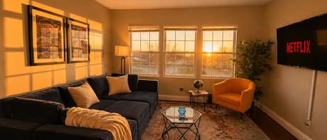 A living room with a sofa, armchair, coffee table, and a TV mounted on the wall.