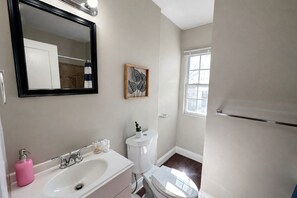 Ein Badezimmer mit einem weißen Waschbecken, einer Toilette, einem Spiegel und einem Fenster.