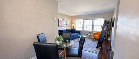 A dining area with a glass table and chairs, a sofa, and a ladder against the wall.