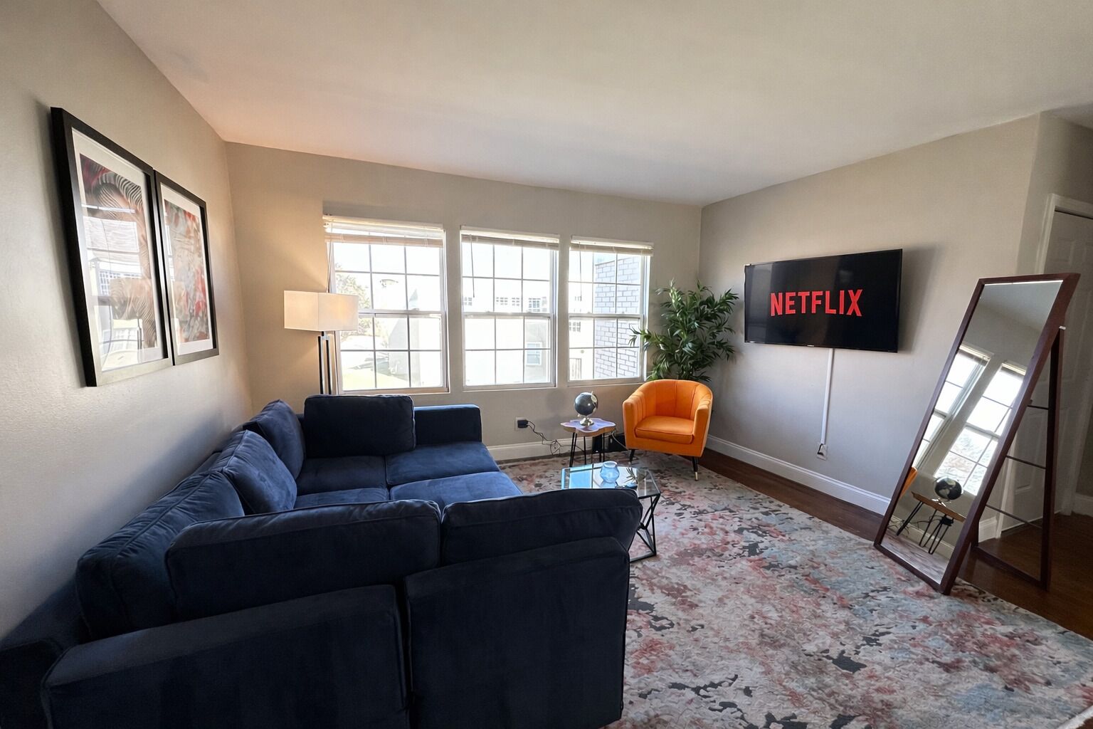 A living room with a sectional sofa, an orange armchair, a flat-screen TV, and a large mirror.