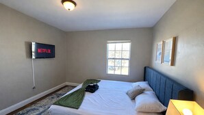 Ein Schlafzimmer mit einem Bett, einem an der Wand montierten Fernseher, einem Fenster und einer Nachttischlampe.