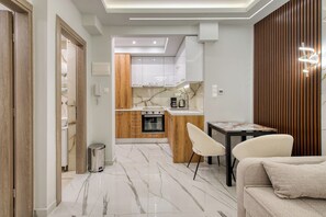 A modern kitchen with a built-in oven, a coffee maker, and a dining area with a table and chairs. - Thessaloniki Retreat - Walk Everywhere by ΜΡS (Thessaloniki)