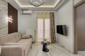 A modern living room with a sofa, a round table with a vase, a flat-screen TV mounted on the wall, and an air conditioning unit. - Thessaloniki Retreat - Walk Everywhere by ΜΡS (Thessaloniki)