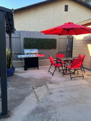 Eine Terrasse mit Grill, roten Stühlen und einem Tisch unter einem roten Sonnenschirm.