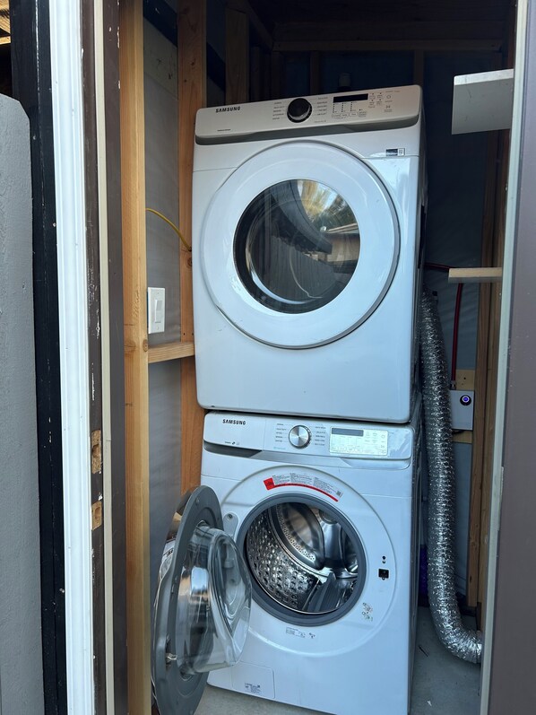 Eine übereinander gestellte Waschmaschine und ein Trockner in einem Raum mit Holzverkleidung und sichtbarer Elektroinstallation.
