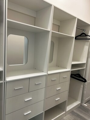 Ein weißer Kleiderschrank mit mehreren Einlegeböden, Schubladen und einer Kleiderstange.