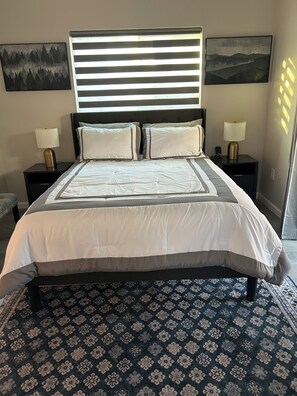 Ein Bett mit Kopfteil, zwei Nachttische mit Lampen, ein gemustertes Teppich und zwei an der Wand hängende Gemälde.
