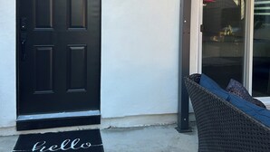 A black door with a welcome mat, a wicker chair, and a glass door. - Cozy Casita in the Valley (Lemon Grove)
