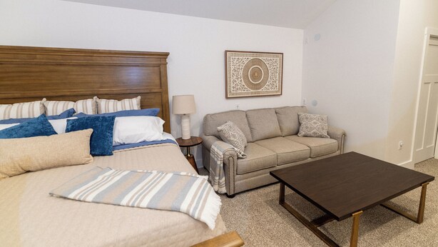 A bedroom with a bed, a nightstand, a sofa, and a coffee table.