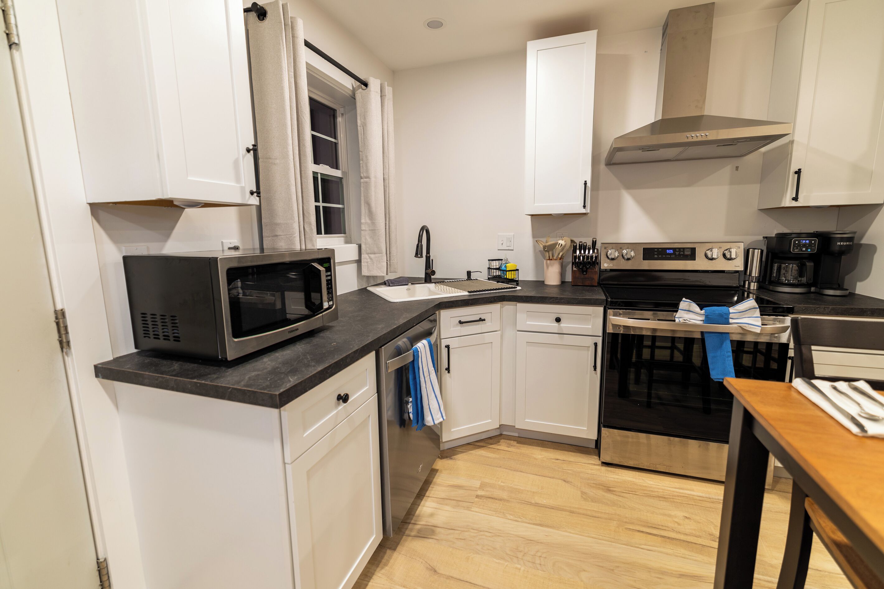 Een moderne keuken met witte kasten, een magnetron, een fornuis en een koffiezetapparaat.